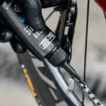 Nahaufnahme einer Hand mit schwarzem Handschuh, die Muc-Off Hydrodynamic Lube auf eine Fahrradkette aufträgt.