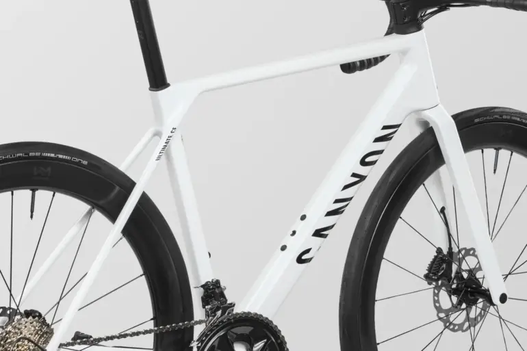 Detailansicht eines weißen Canyon Ultimate CF 7 A.50 Rennrads, Fokus auf den Carbonrahmen, die Kurbelgarnitur und das Hinterrad.