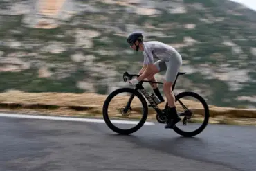 Radfahrer fährt schnelles Aero-Rennrad Giant Propel Advanced Pro auf kurviger Straße mit Bergkulisse.