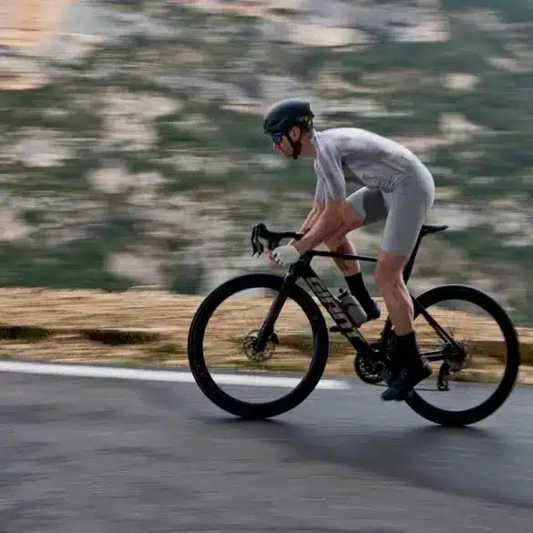 Radfahrer fährt schnelles Aero-Rennrad Giant Propel Advanced Pro auf kurviger Straße mit Bergkulisse.