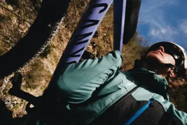 Nahaufnahme einer Frau mit Helm, die auf einem Fahrrad sitzt und ein grün-blaues Longsleeve von Millet trägt, im Hintergrund ein Fahrradrahmen mit der Aufschrift "CANYON".