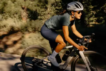 Eine Frau fährt ein Specialized Turbo Creo 2 Expert E-Gravelbike auf einem sonnigen Schotterweg, umgeben von Bäumen und Vegetation.