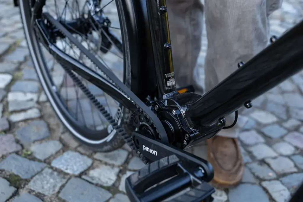 Nahaufnahme des schwarzen Stevens Caleta 9.2 LT Trekkingrads, Fokus auf das Pinion-Getriebe, die Pedale und den Gates Carbon-Riemen.