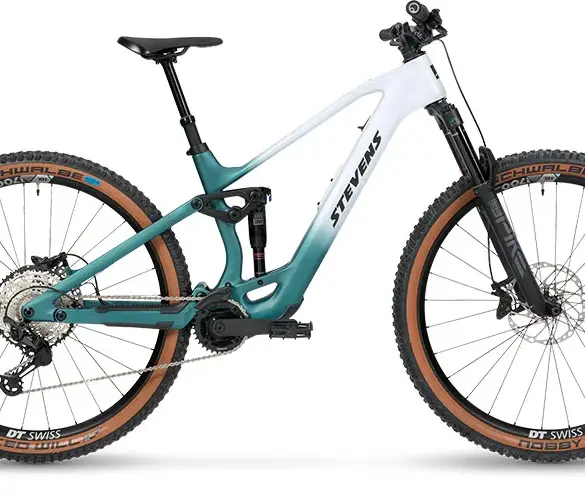 Seitenansicht des Stevens E-Maverick AM 7.4.3, einem weißen und türkisfarbenen E-Mountainbike mit Carbonrahmen und braunen Reifen.