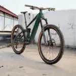 Seitenansicht eines dunkelgrünen Maxx Fab.4 Ela E-Enduro Fahrrads, das auf einem Betonboden steht.