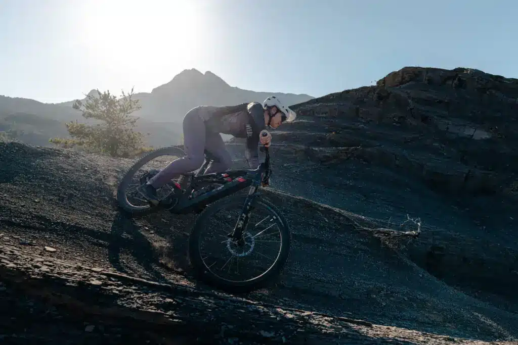 Fahrer auf einem schwarzen ROTWILD R.XX E-Trailbike mit roten Akzenten fährt bergab auf einem felsigen Hang mit Blick auf Berge im Hintergrund.