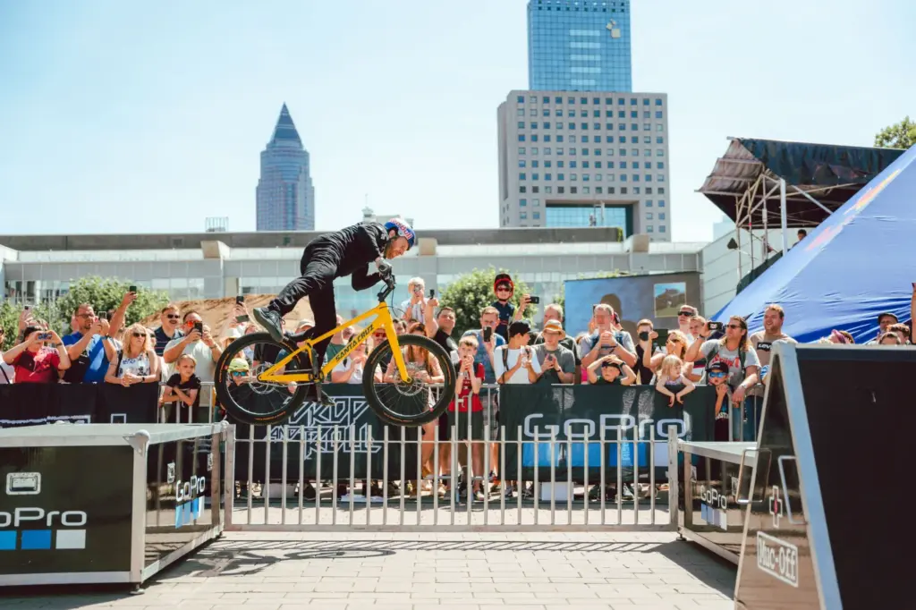 BMX-Fahrer in Aktion während eines Sprungs über ein Hindernis auf der Eurobike Messe, umgeben von einer jubelnden Menge.