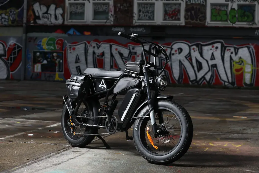 Schwarzes CAVET Air E-Bike mit breiten Reifen, langem Sattel und Gepäcktaschen, parkend vor einer auffälligen Graffiti-Wand.
