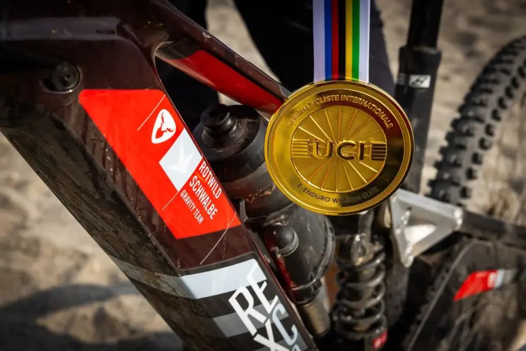 Nahaufnahme des Rahmens eines ROTWILD R.EXC E-Enduro-Mountainbikes, geschmückt mit einer goldenen UCI E-Enduro Weltmeistermedaille, die über dem Hauptrahmen hängt.