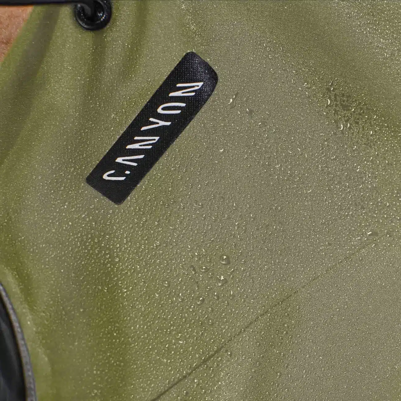 Nahaufnahme einer olivgrünen Canyon Fahrrad Regenjacke mit sichtbaren Wassertropfen und Canyon-Logo