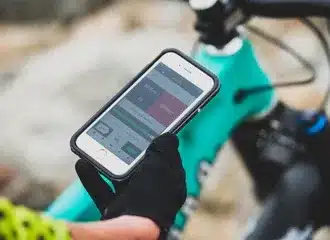 Hand mit Smartphone, das die ShockWiz App neben einem Mountainbike bedient