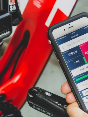 Smartphone mit geöffneter ShockWiz-App neben einem Mountainbike mit installiertem ShockWiz-Gerät