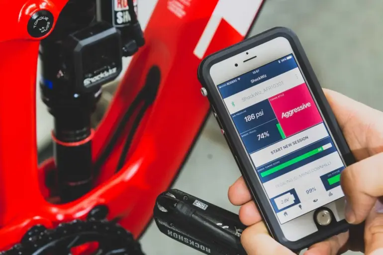Smartphone mit geöffneter ShockWiz-App neben einem Mountainbike mit installiertem ShockWiz-Gerät