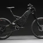 Seitenansicht eines "2024 Revolution" Downhill E-Bikes von Hi-Power Cycles mit auffälliger Carbon-Optik am Rahmen, breiten Reifen und Federung.