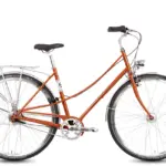 Ein Böttcher Ditmarsia Swing Fahrrad in der auffälligen Farbe Perlorange, mit elegant geschwungenem Stahlrahmen, Gepäckträger und Retro-LED-Scheinwerfer, isoliert auf weißem Hintergrund.