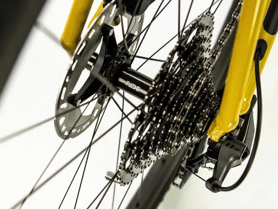 Detailaufnahme des Hinterrads eines gelben Böttcher Gravel-E SX Elektro-Gravelbikes, mit Fokus auf die Kassette mit 11 Gängen und die hydraulische Scheibenbremse.