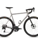 Ein Böttcher Titanium Endurance Diamant Fahrrad, das für Langstreckenfahrten konzipiert ist, wird auf weißem Hintergrund präsentiert. Das Fahrrad ist in Silbermetallic gehalten und verfügt über einen robusten Titanrahmen mit einer eleganten Geometrie. Es ist mit einer Shimano GRX Gruppe, Scheibenbremsen und breiten Continental Terra Speed Reifen ausgestattet, die auf Carbonfelgen montiert sind.
