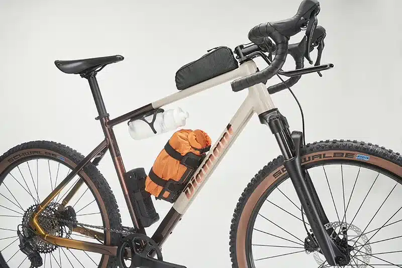 Seitenansicht eines Diamant 140 Gravelbikes mit montiertem Gepäckträger vorne, Wasserflasche, orangefarbener Gepäckrolle und Rahmentasche.