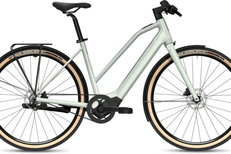 Das FLYER Upstreet SL 3.63 Trapez E-Bike in seitlicher Ansicht mit hellem Rahmen, Riemenantrieb, Schutzblechen und Gepäckträger