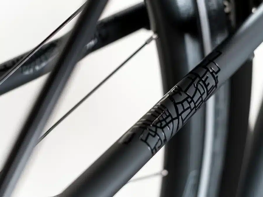 Detailaufnahme des Rahmens eines schwarzen Grecos Urban Belt Diamant Fahrrads, das ein stilisches Logo zeigt.