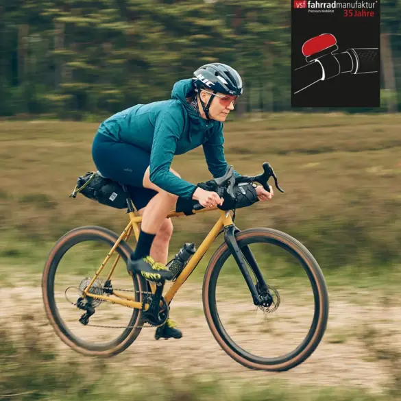 Fahrerin auf dem GX-1200 1st Edition Gravelbike der vsf fahrradmanufaktur mit Dirty-Mustard-Lackierung, unterwegs auf einem Schotterweg