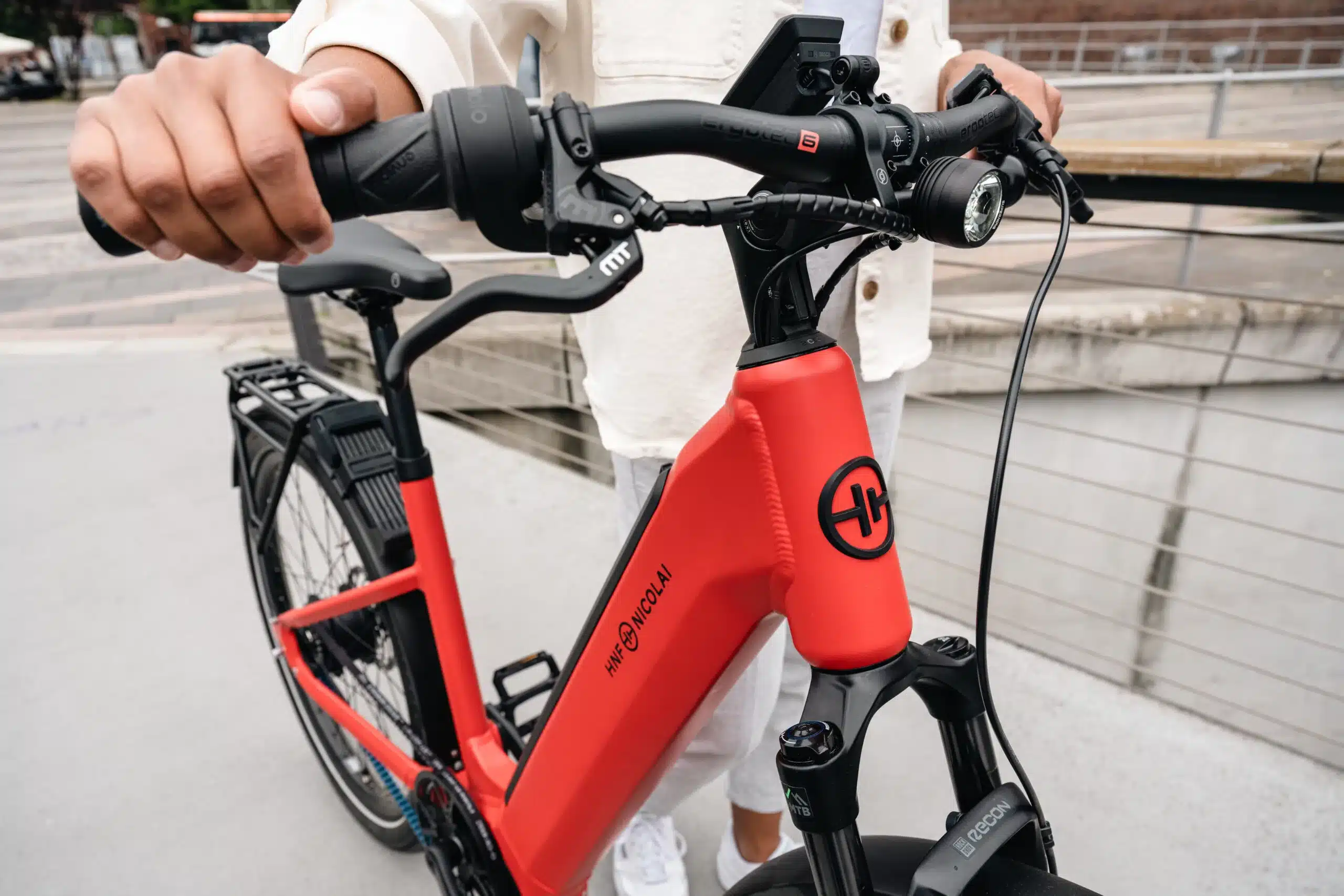 Eine Person hält den Lenker eines roten HNF Nicolai UD4 E-Bikes. Der Fokus liegt auf dem roten Rahmen mit dem HNF Nicolai Logo und den Bedienelementen.