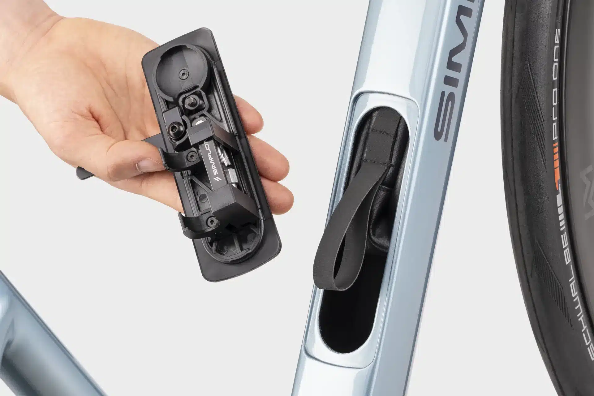 Hand hält ein aus dem Unterrohr entnehmbares Multitool-Set. Das Staufach im Rahmen des Simplon Kiaro Rennrads ist geöffnet.