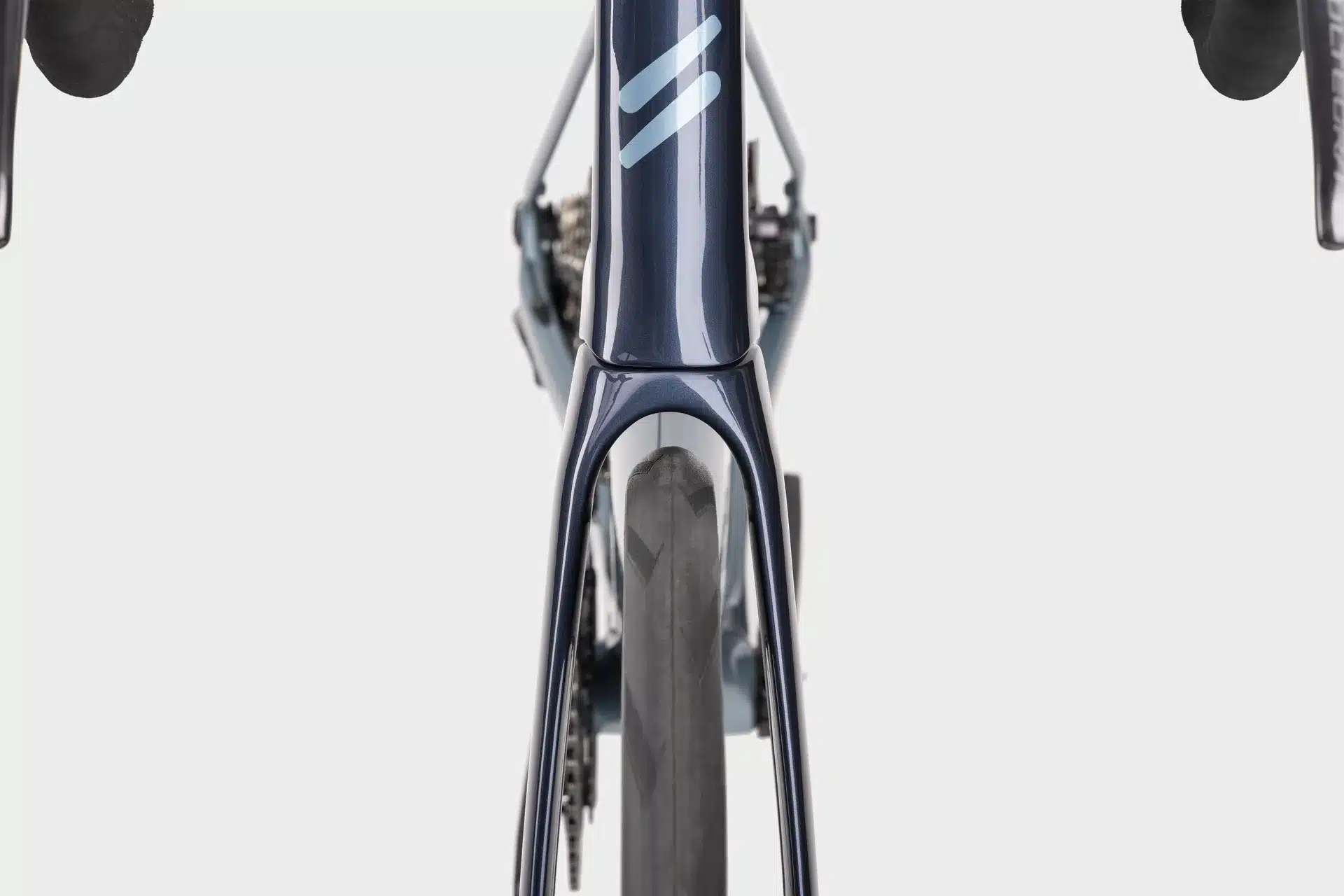 Nahaufnahme des vorderen Teils eines Simplon Kiaro Endurance-Rennrads, gesehen von oben. Der dunkle Carbonrahmen mit dem Simplon-Logo in Hellblau ist zu sehen, ebenso wie die Gabel, das Vorderrad und Teile der Lenker