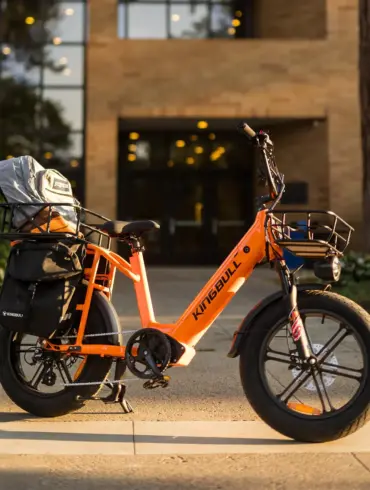 Ein orangefarbenes Kingbull Voyager 2.0 E-Bike mit breiten Reifen und Gepäckaufbauten steht im Freien vor einem Gebäude.