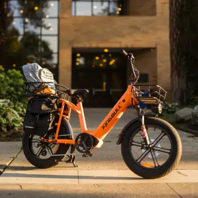 Ein orangefarbenes Kingbull Voyager 2.0 E-Bike mit breiten Reifen und Gepäckaufbauten steht im Freien vor einem Gebäude.