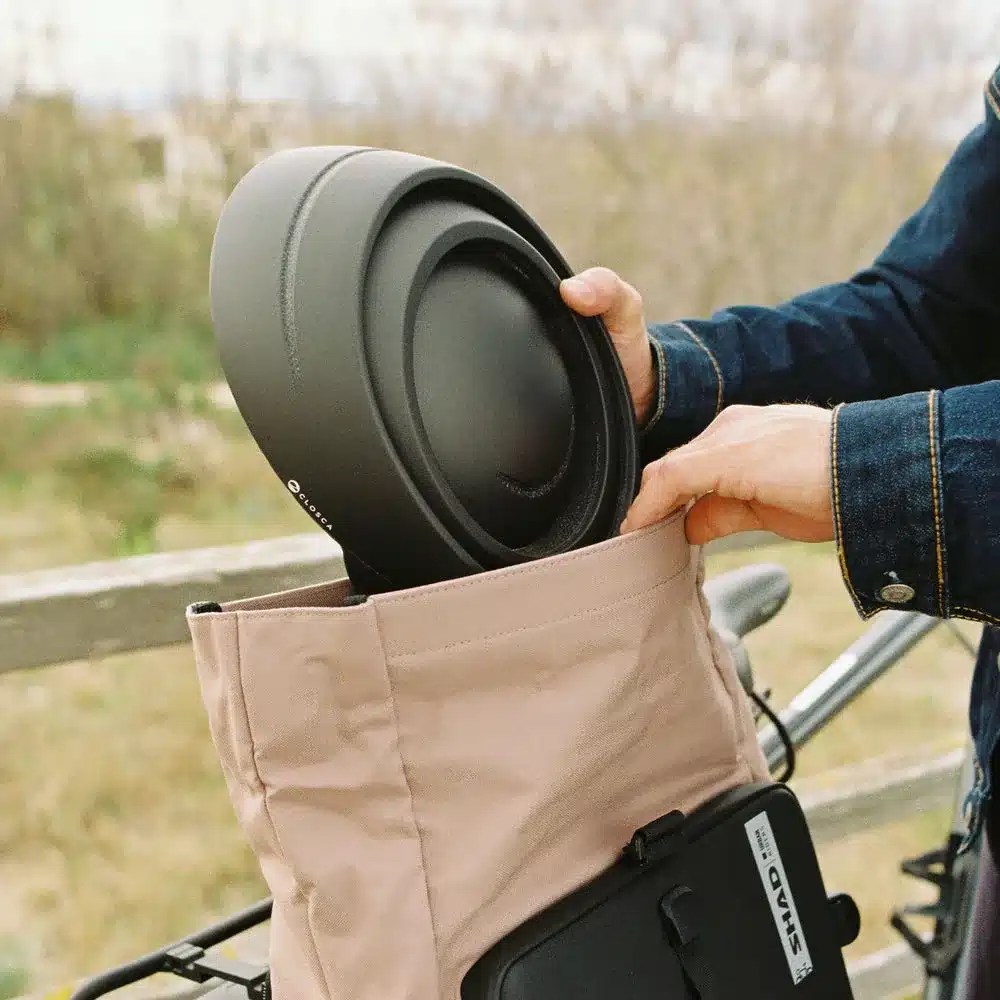 Person verstaut einen schwarzen faltbaren Fahrradhelm von Closca in eine beigefarbene Tasche