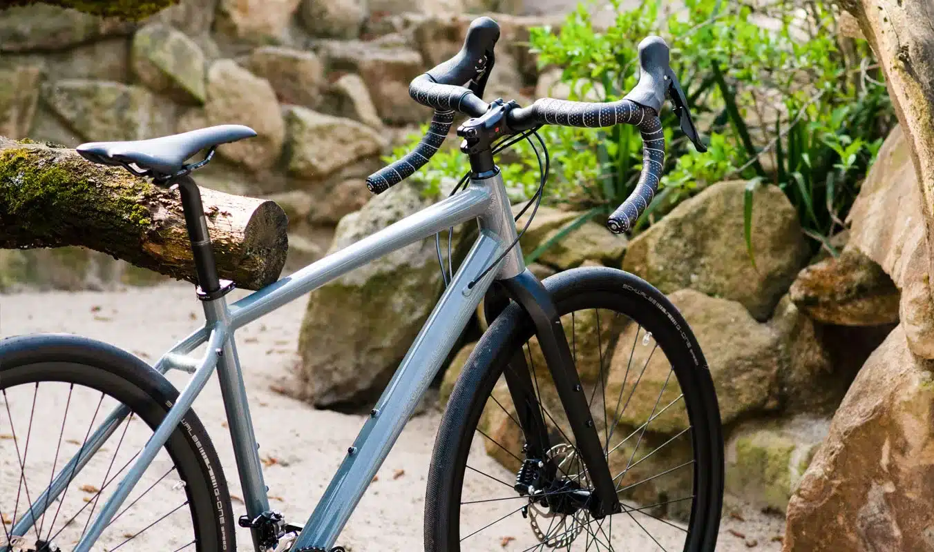 Silbernes Maxcycles Gravel Lite Fahrrad im Freien, Fokus auf Rahmen, Lenker und Vorderreifen.