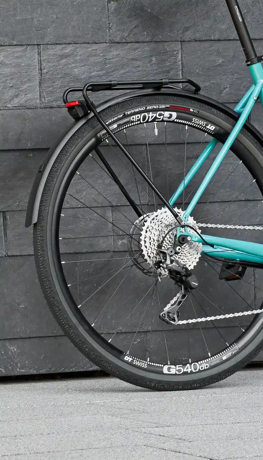 Detailaufnahme des Hinterrads eines turquoisefarbenen Tout Terrain Nolita Fahrrads mit schwarzen Schutzblechen und Gepäckträger.