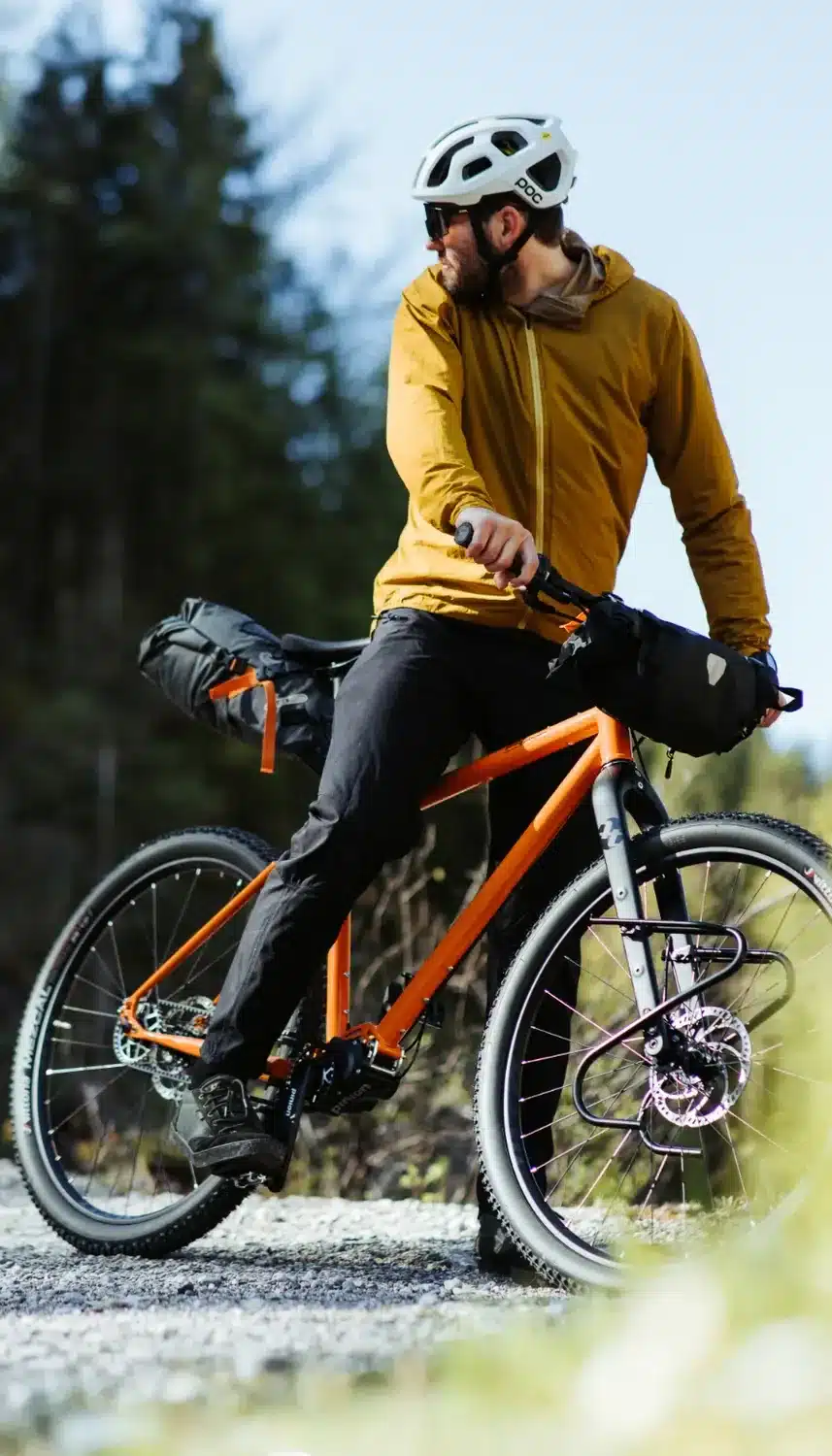 Mann auf einem orangen Tout Terrain Outback Fahrrad mit Gepäckträgern und Satteltaschen, bereit für Offroad-Abenteuer.