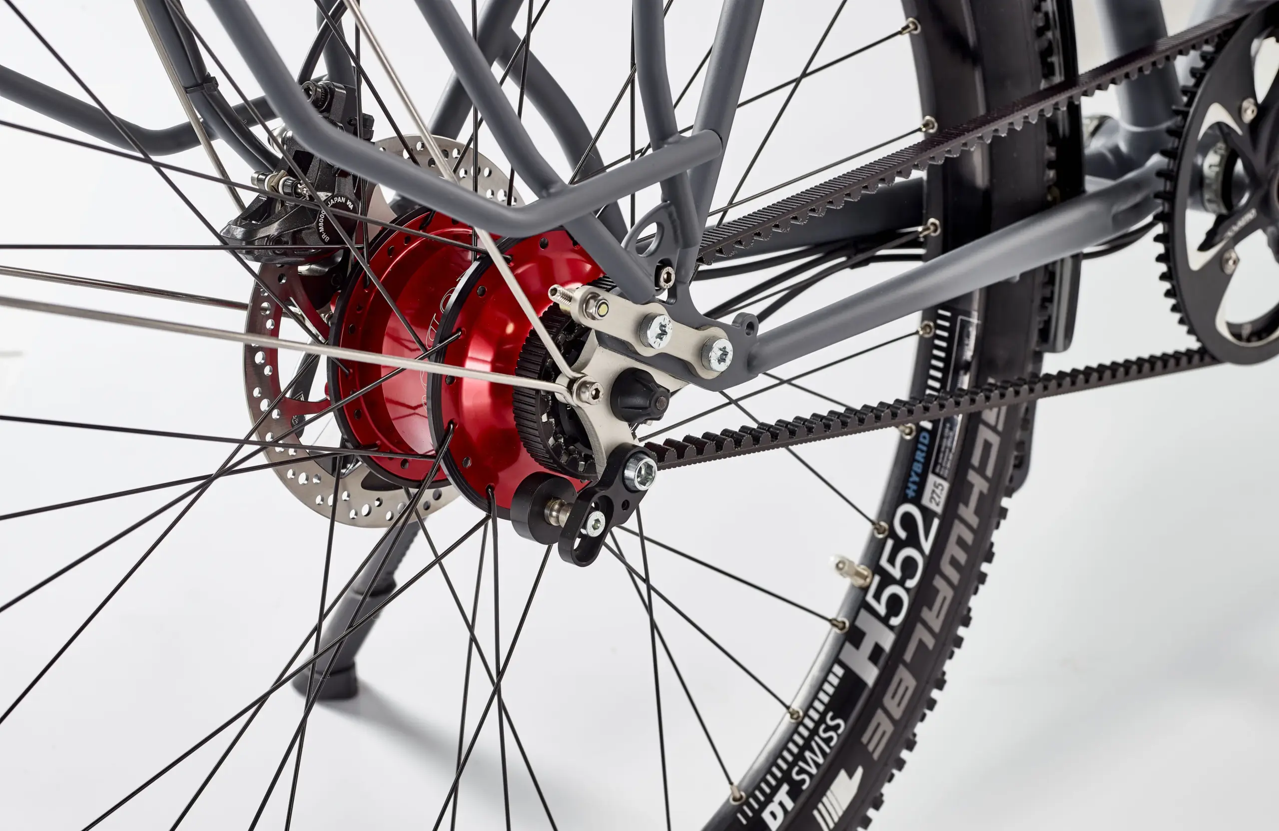 Nahaufnahme des Hinterrads eines Patria Kosmos Reiserads, das einen Gates Carbon Drive Riemenantrieb, eine Scheibenbremse und einen roten Nabendynamo zeigt.