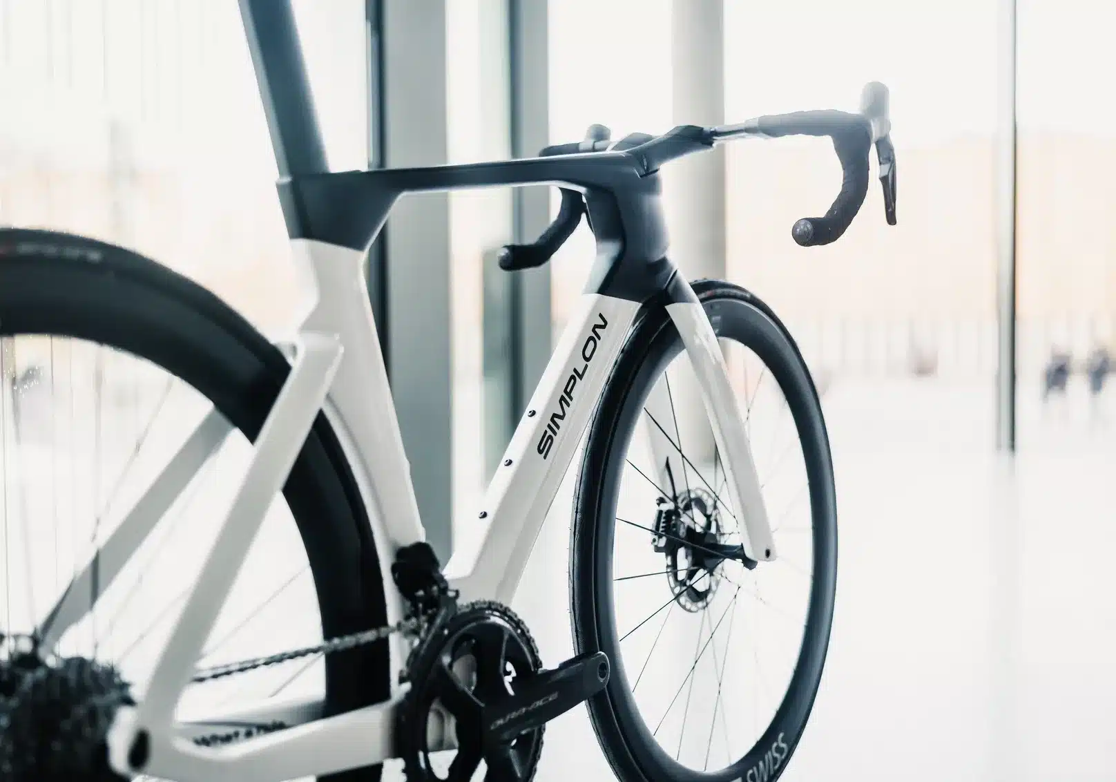 Nahaufnahme eines weißen Simplon PRIDE Rennrads mit schwarzen Akzenten, Fokus auf den aerodynamischen Rahmen, den integrierten Vorbau und das Vorderrad.