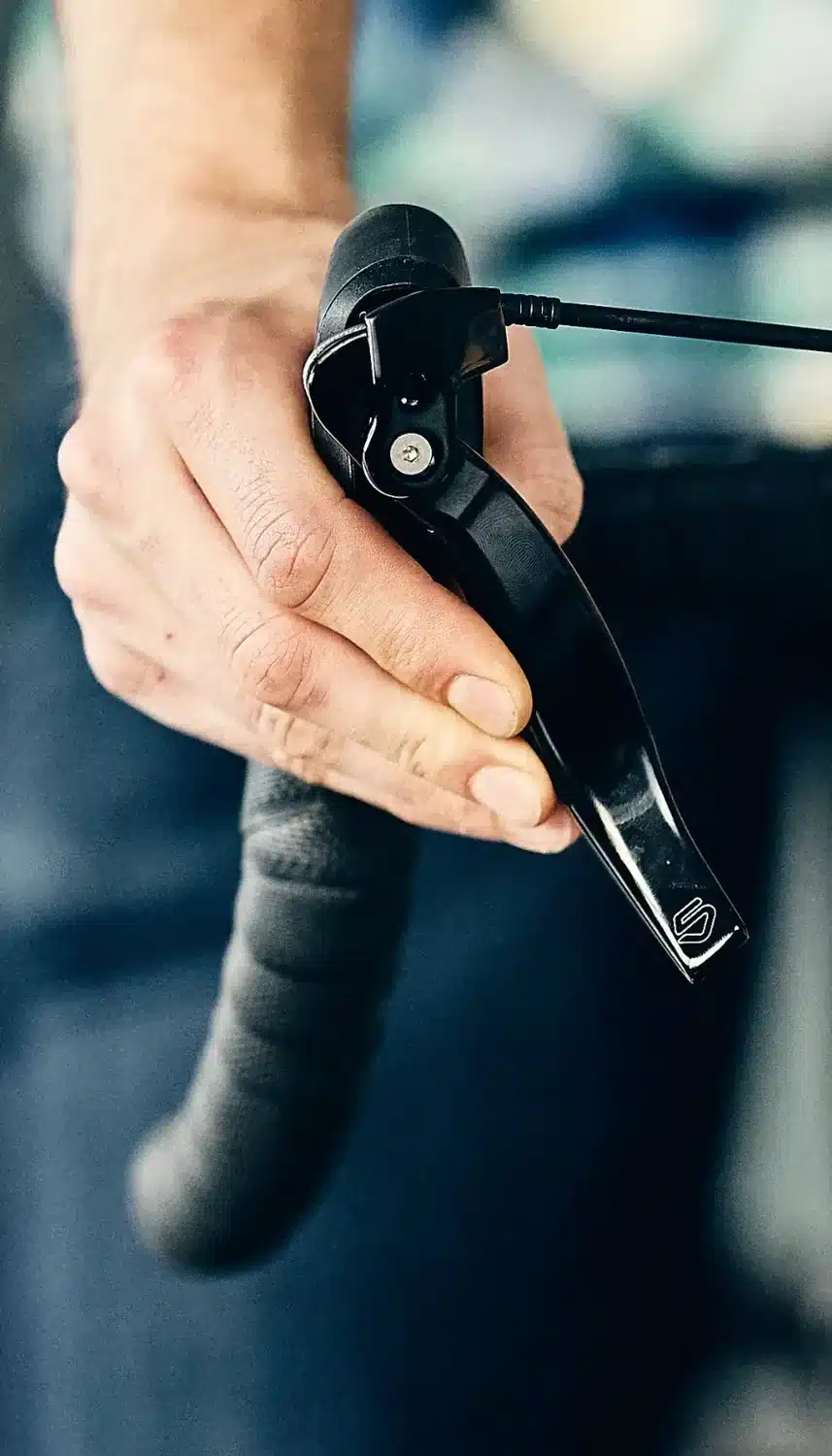 Nahaufnahme einer Hand, die einen schwarzen Fahrradbremshebel betätigt.