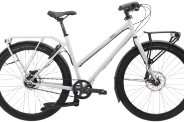 Schwarzes Tout Terrain Shopper Fahrrad mit Gepäckträgern vorne und hinten, Scheibenbremsen und Riemenantrieb auf weißem Hintergrund.