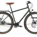 Dunkelgrünes Tout Terrain Tourenrad Silkroad mit braunem Ledersattel, Gepäckträgern vorne und hinten sowie einem Pinion-Mittendrive-Getriebe.