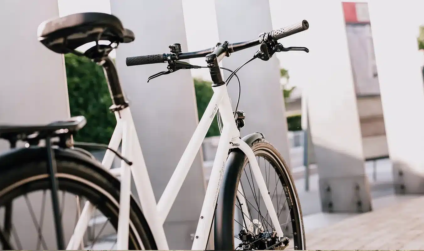 Detailaufnahme eines weißen Steel Lite 2 Trapez Fahrrads mit Fokus auf den Lenker, das Vorderrad und den Rahmen.