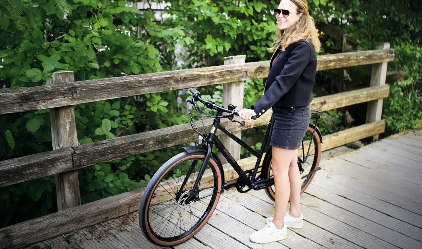 Schwarzes Steel Lite 2 Trapez Fahrrad mit Frau, stehend auf einem Holzsteg im Freien.