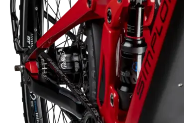 Detailaufnahme des Hinterrads eines roten SIMPLON Stomp SUV :e E-Mountainbikes mit Fokus auf den Rohloff Nabenschalter und den Gates Carbon Drive Riemenantrieb sowie den RockShox Dämpfer.