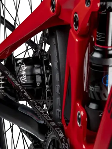Detailaufnahme des Hinterrads eines roten SIMPLON Stomp SUV :e E-Mountainbikes mit Fokus auf den Rohloff Nabenschalter und den Gates Carbon Drive Riemenantrieb sowie den RockShox Dämpfer.