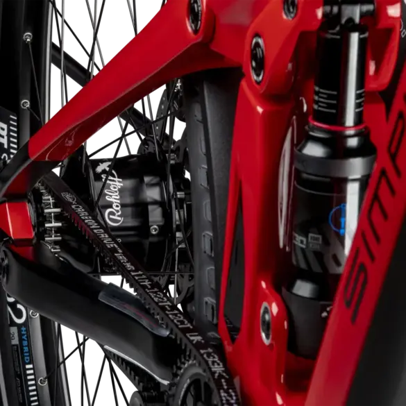 Detailaufnahme des Hinterrads eines roten SIMPLON Stomp SUV :e E-Mountainbikes mit Fokus auf den Rohloff Nabenschalter und den Gates Carbon Drive Riemenantrieb sowie den RockShox Dämpfer.