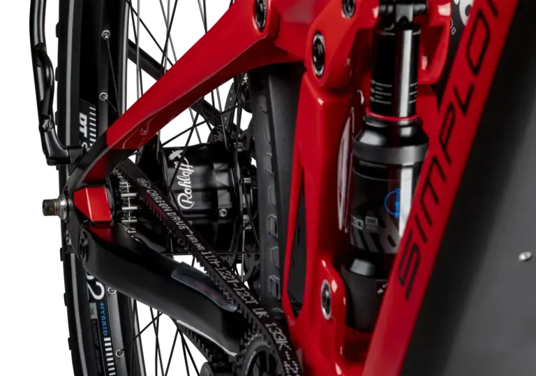 Detailaufnahme des Hinterrads eines roten SIMPLON Stomp SUV :e E-Mountainbikes mit Fokus auf den Rohloff Nabenschalter und den Gates Carbon Drive Riemenantrieb sowie den RockShox Dämpfer.