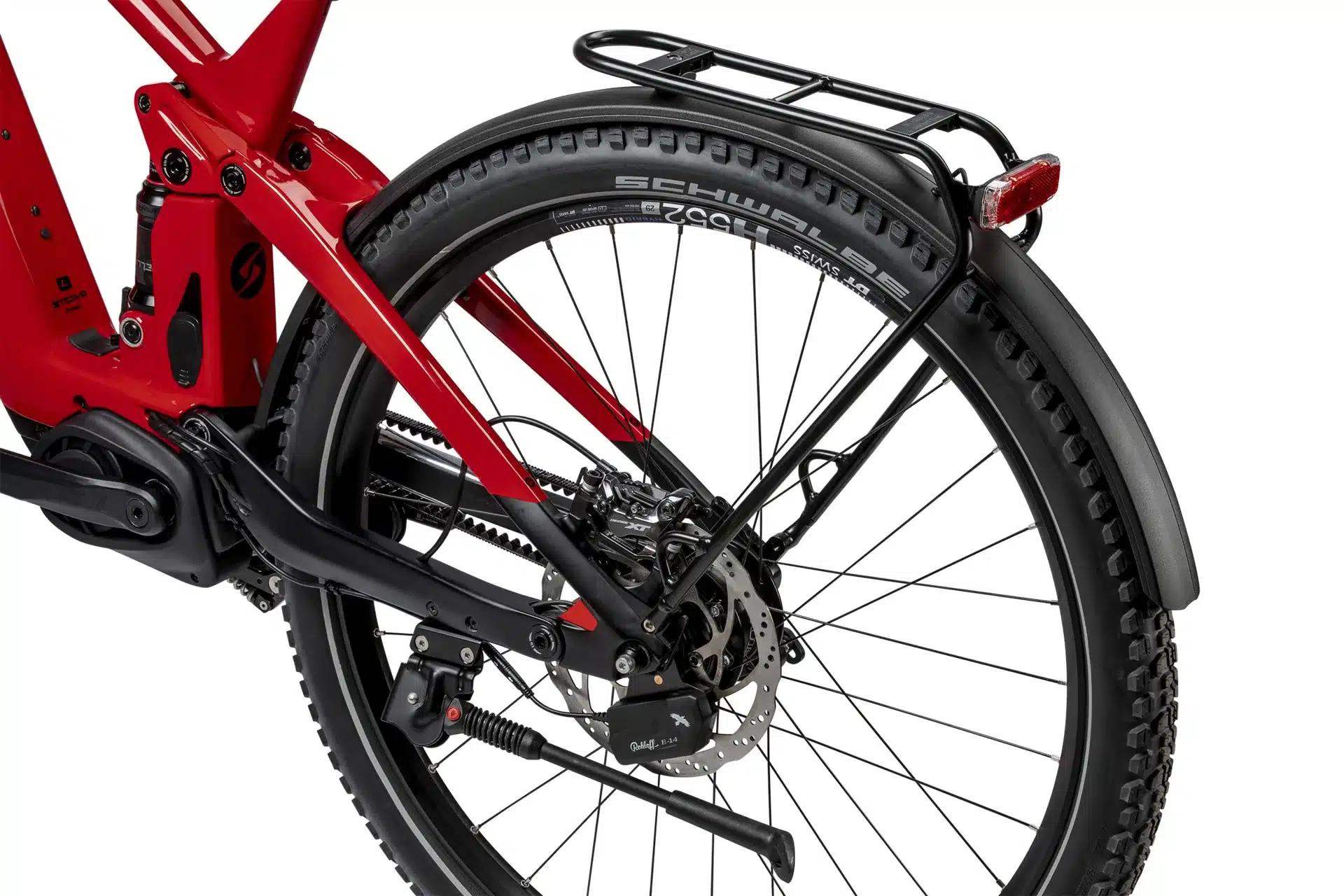 Nahaufnahme des Hinterrads eines roten SIMPLON Stomp SUV :e E-Mountainbikes, mit Fokus auf die Federung, den Antriebsriemen, die Scheibenbremse und den montierten Gepäckträger.