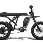 Seitenansicht des SUPER73-R Adventure Core Elektrofahrrads in Grau und Schwarz, mit Fokus auf den vollgefederten Rahmen, die breiten Offroad-Reifen und den seitlich angebrachten Akku.