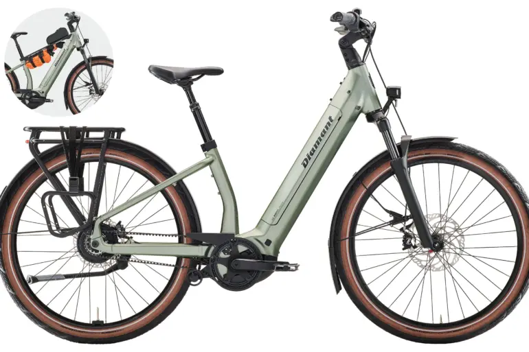 Hellgrünes Diamant Suvea Style 600 Wh Touren-E-Bike mit schwarzem Gepäckträger und orangefarbenen Packsäcken am Lenker.