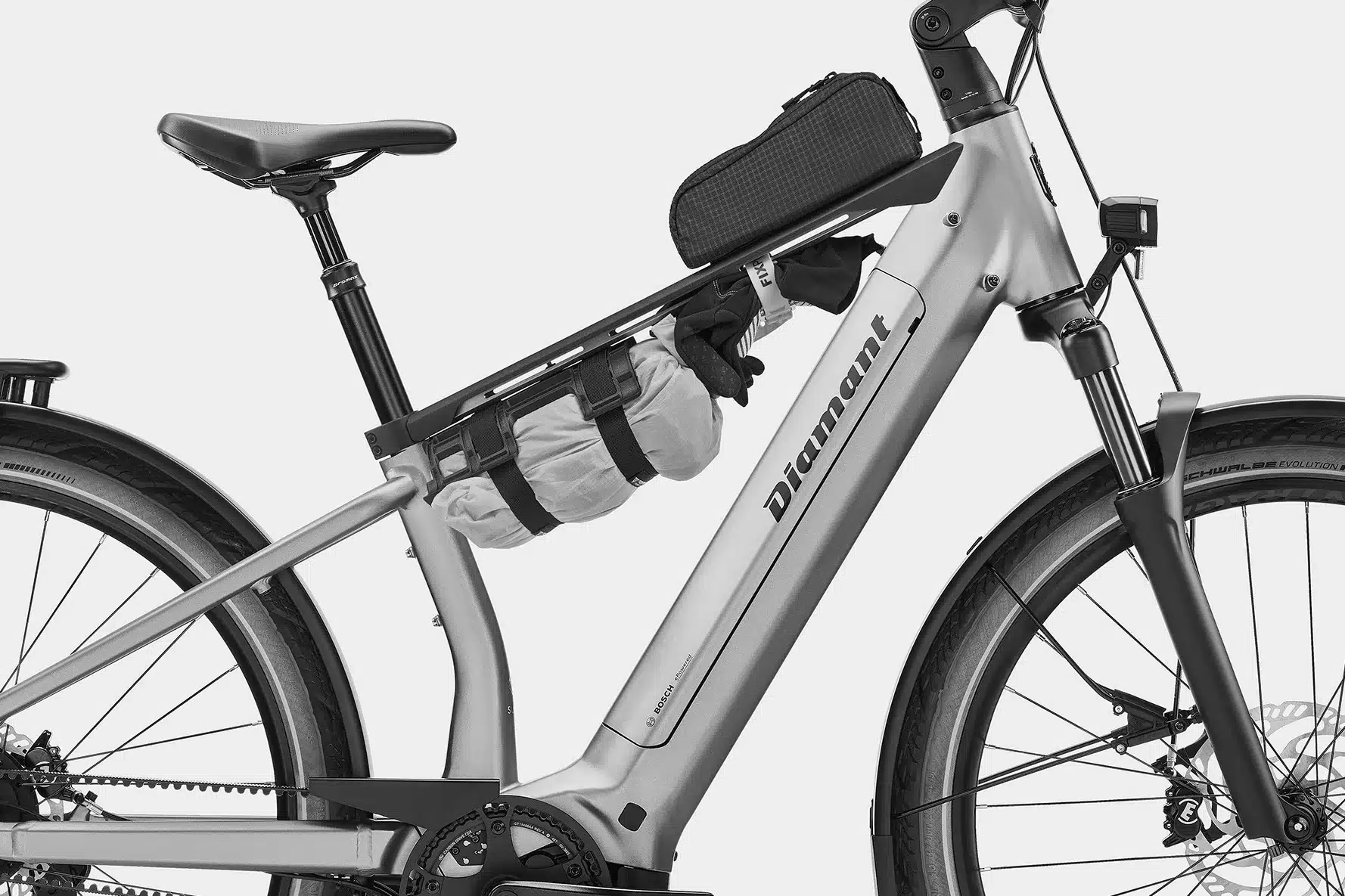 Detailansicht des silbernen Suvea Style 600 Wh Touren-E-Bikes mit Fokus auf den Rahmen, die Gepäckhalterung mit daran befestigten Taschen und Handschuhen sowie dem Bosch Smart System Motor.
