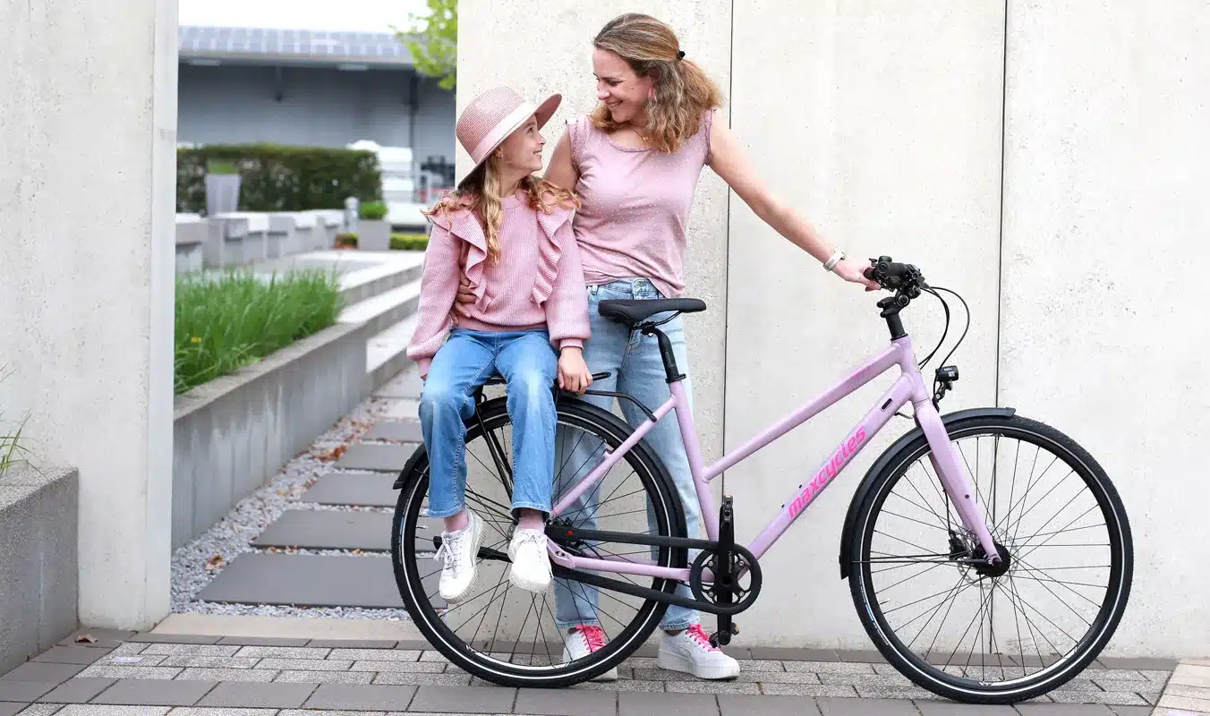 Maxcycles Traffix 2 Stadtrad in Hellviolett mit einer Frau und einem Kind daneben.